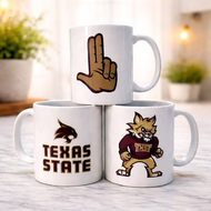 Three white mugs with Texas State logos stacked on a wooden surface.
